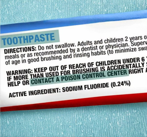 Close-up image of a fluoride toothpaste package displaying sodium fluoride (0.24%) as the active ingredient and a Poison Control warning if swallowed. Educational visual discussing fluoride toothpaste ingredients, oral health safety, consumer awareness, and toothpaste warning labels.